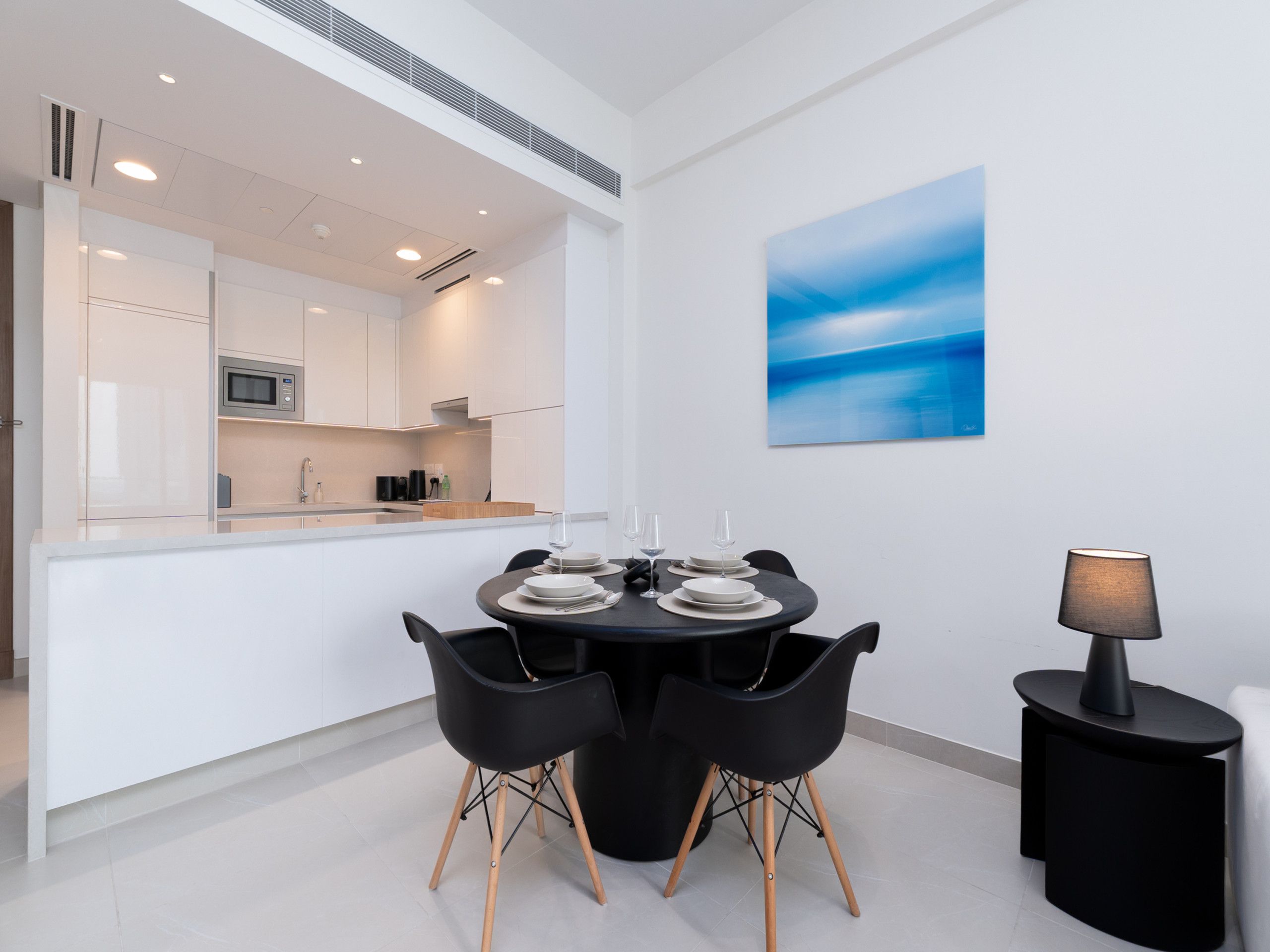 A modern dining area with a round table, black chairs, and a side table with a lamp.