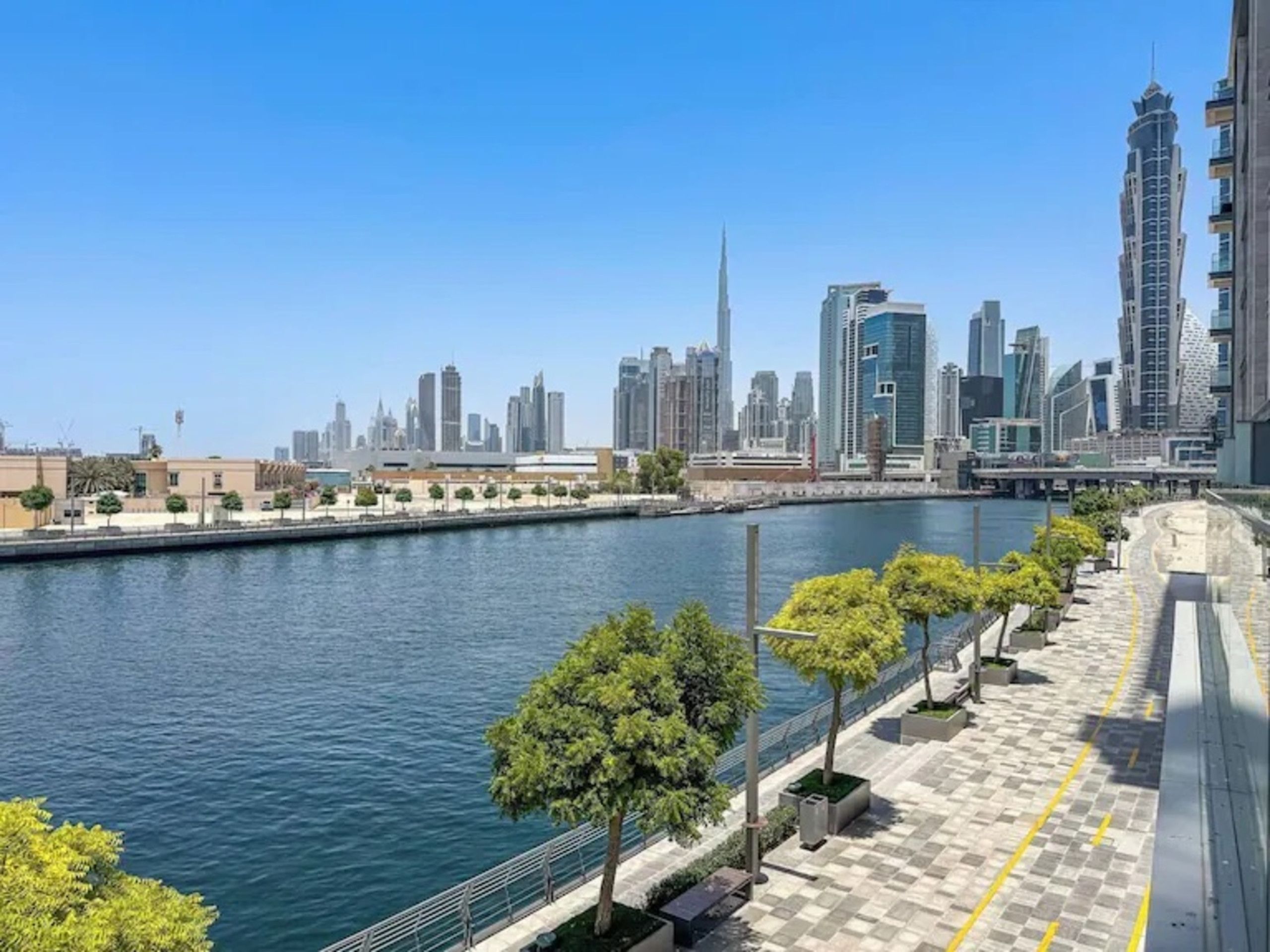 A waterfront promenade with a city skyline in the background, including a prominent skyscraper.