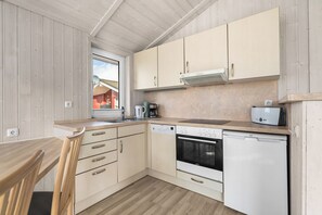A compact kitchen with wooden cabinets, a built-in oven, a dishwasher, and a window overlooking a red building. - Baltic Aloha Hus: A Holiday Home 250 m from Grömitz Beach (Grömitz)