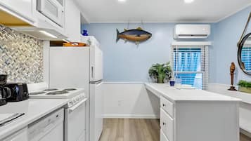 A modern kitchen with white cabinetry, a fish hanging on the wall, and a window with blue shutters.