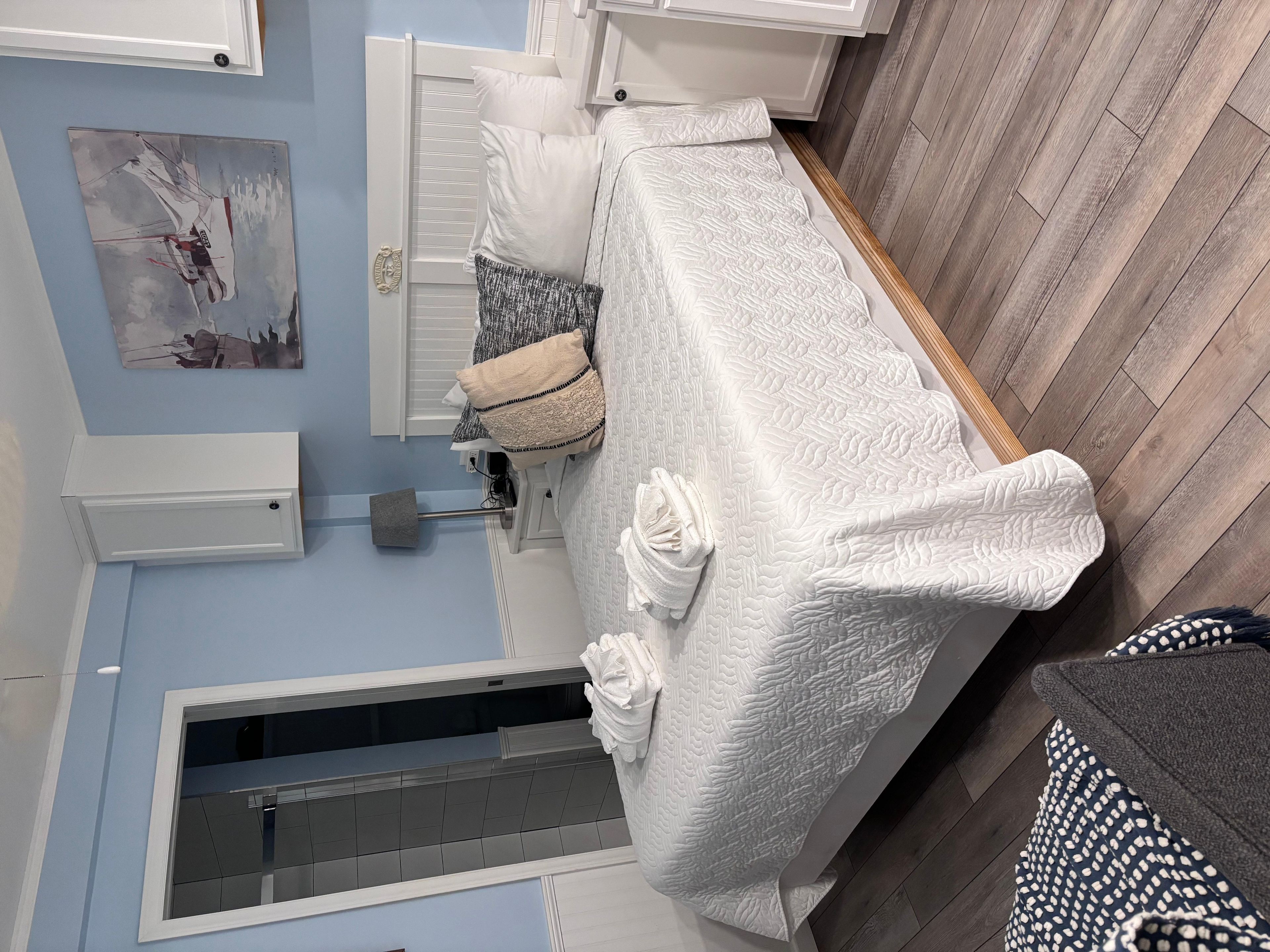 A room with a bed, a window, a painting, and a wooden floor.