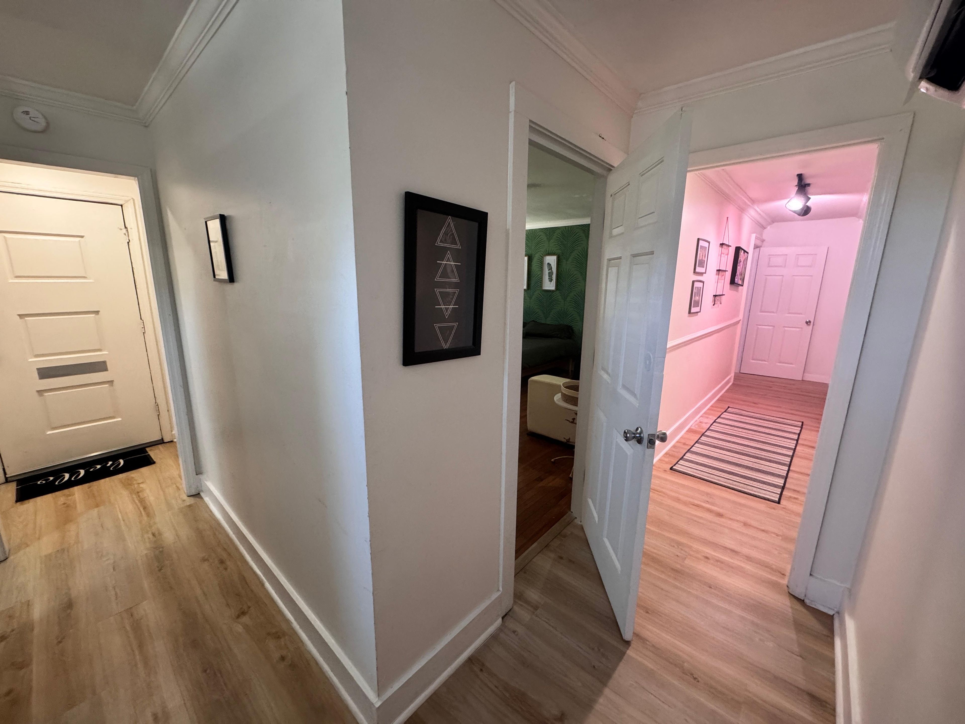 Un couloir doté d’un plancher en bois, de murs blancs et d’une porte donnant sur une pièce avec un mur vert et un lit.