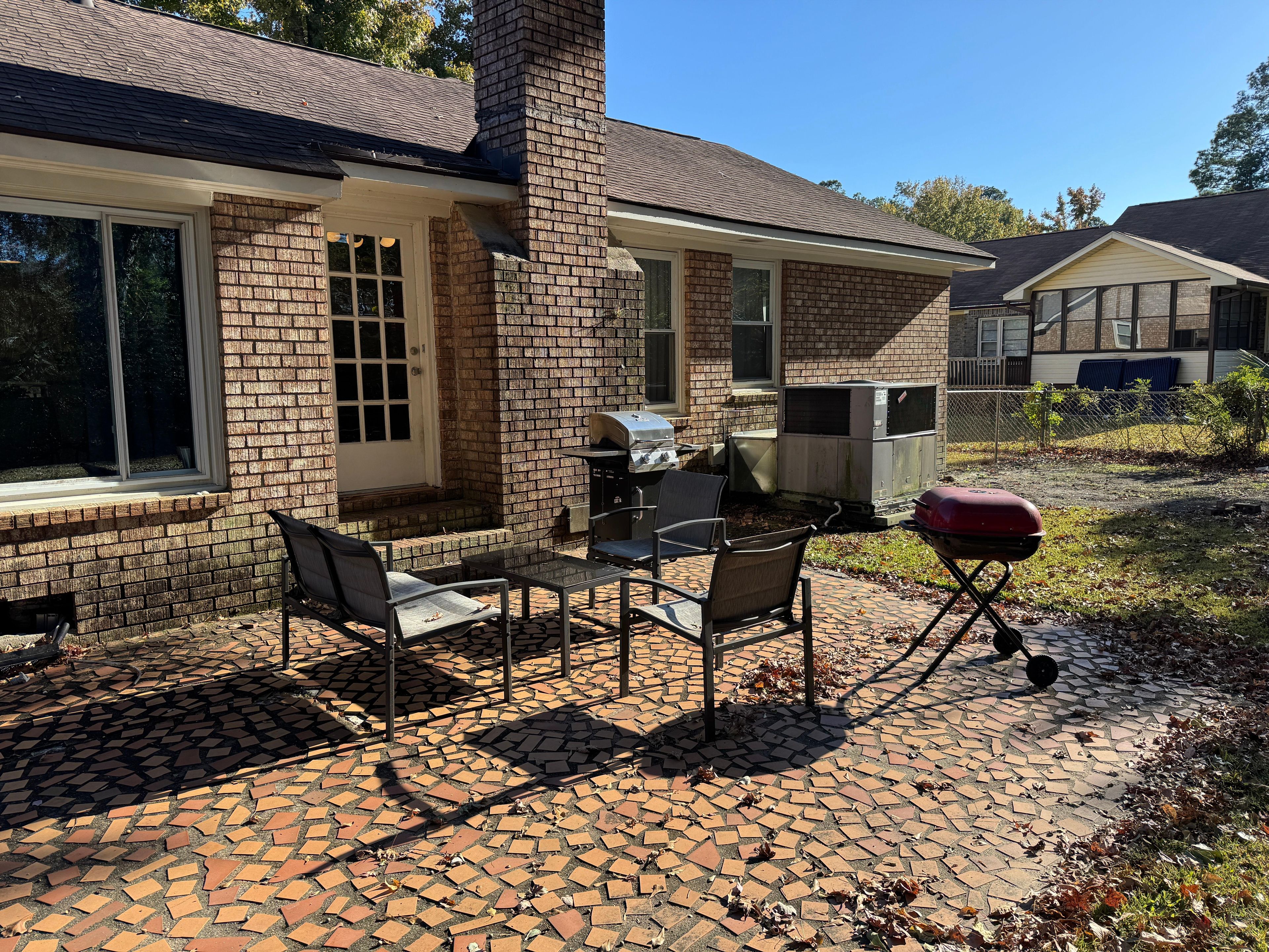 Eine Terrasse mit Ziegelböden, Gartenmöbeln und einem Grill.
