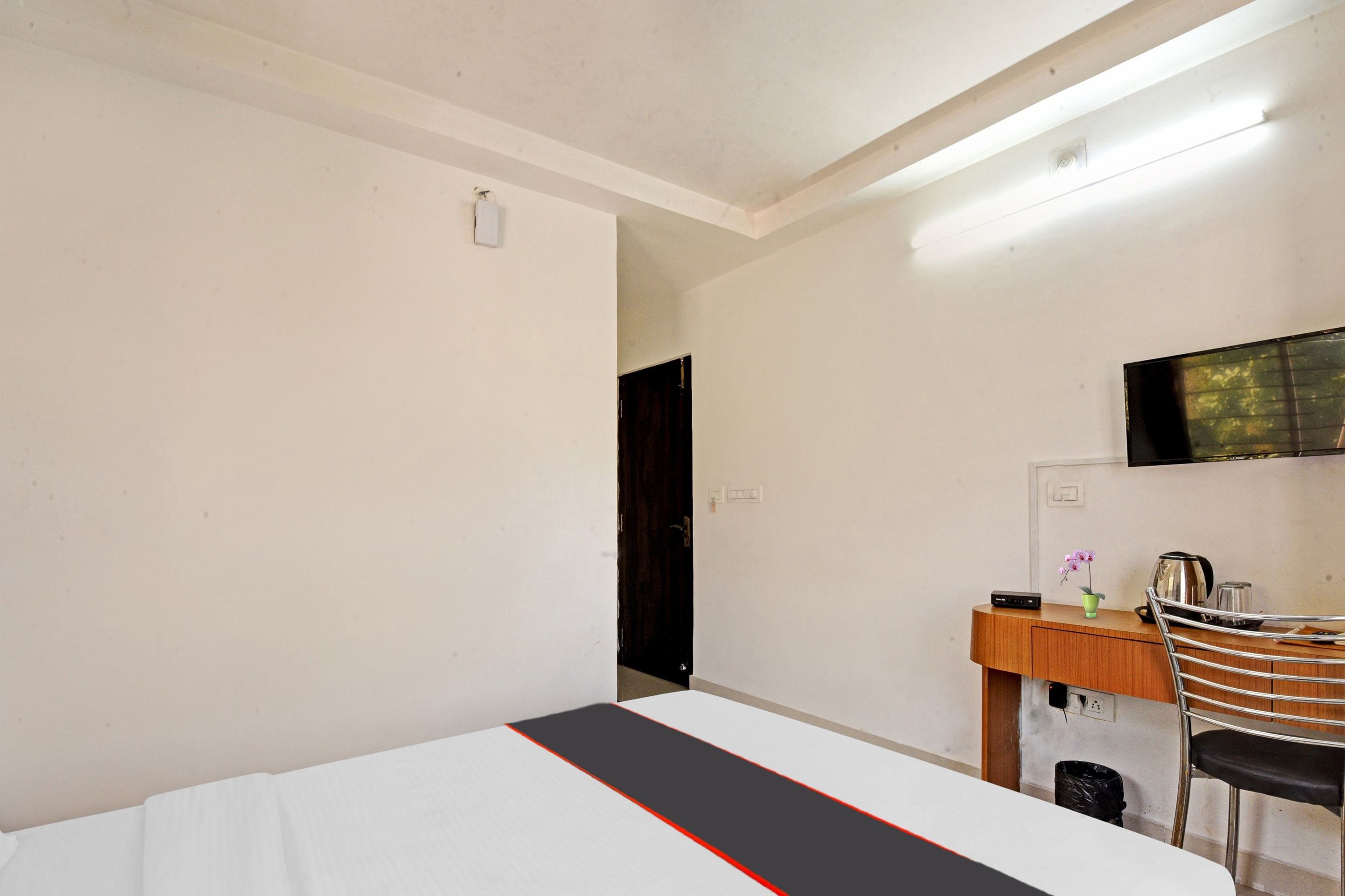 Habitación de hotel con cama, escritorio, silla, televisor y una mesita con un florero.