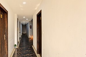 A hallway with a marble floor, wooden doors, and recessed ceiling lights. - Collection O Mountain View Resort (Ranchi)