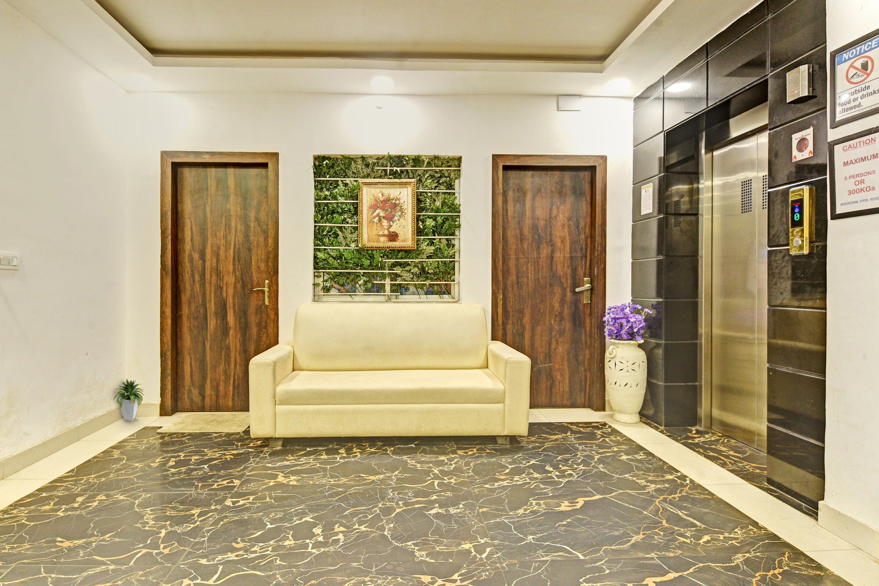 A lobby with a marble floor, a sofa, two wooden doors, a wall-mounted picture, and a refrigerator with a sign.