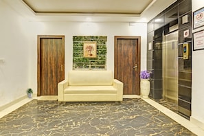 A lobby with a marble floor, a sofa, two wooden doors, a wall-mounted picture, and a refrigerator with a sign.