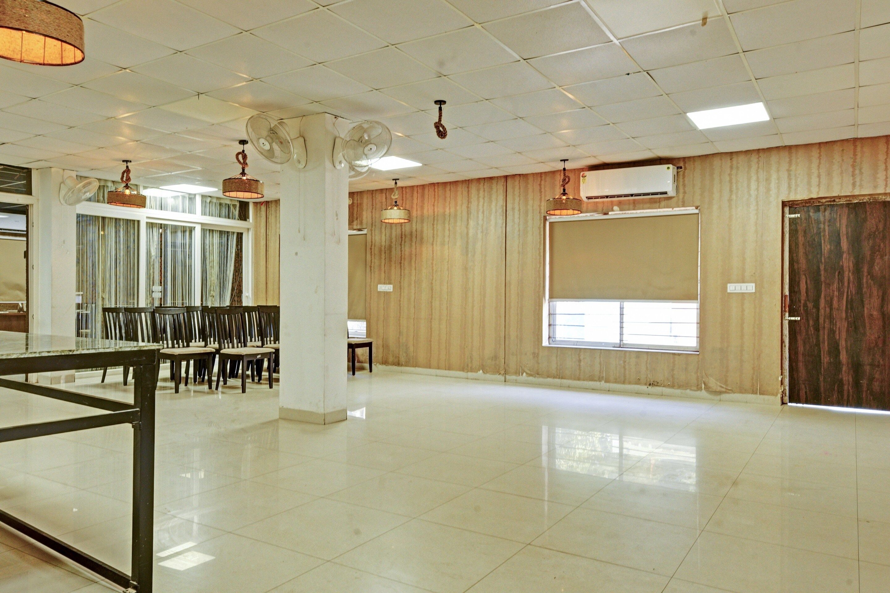 A spacious room with a tiled floor, a large window, and a door. There are ceiling fans and a hanging light fixture.