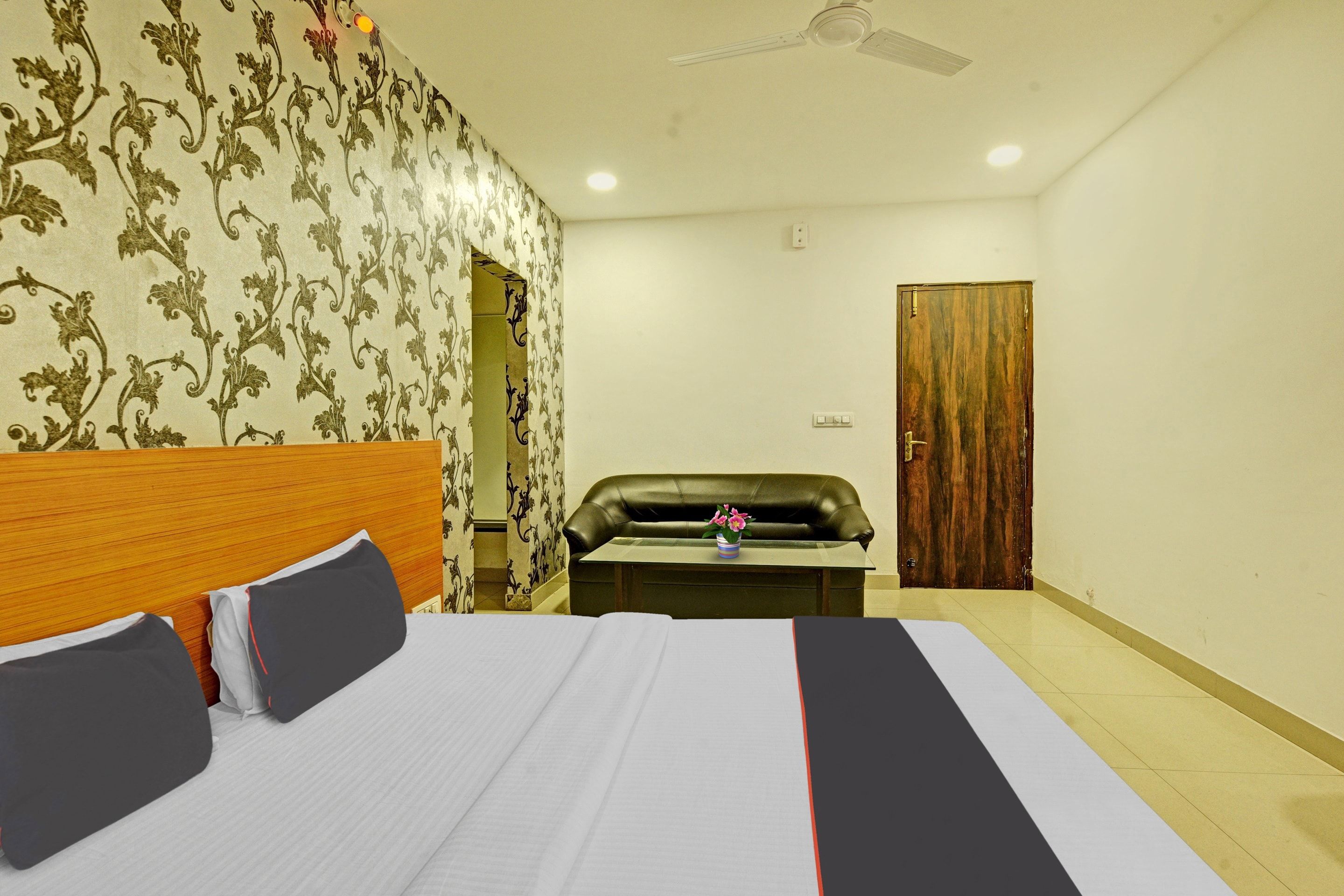 Habitación de hotel con cama, escritorio, sofá de cuero, puerta de madera y papel tapiz estampado.