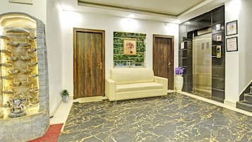 A reception area with a marble floor, a sofa, a decorative wall, and an elevator.
