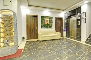 Zona de recepción con suelo de mármol, un sofá, una pared decorativa y un ascensor.
