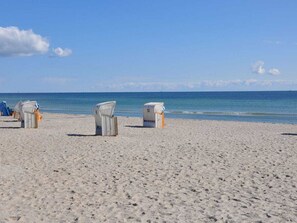 A beach with white beach chairs and umbrellas, a clear sky, and a calm sea. - Holiday Home "marinaperle" at Kai 29 A (Grossenbrode)