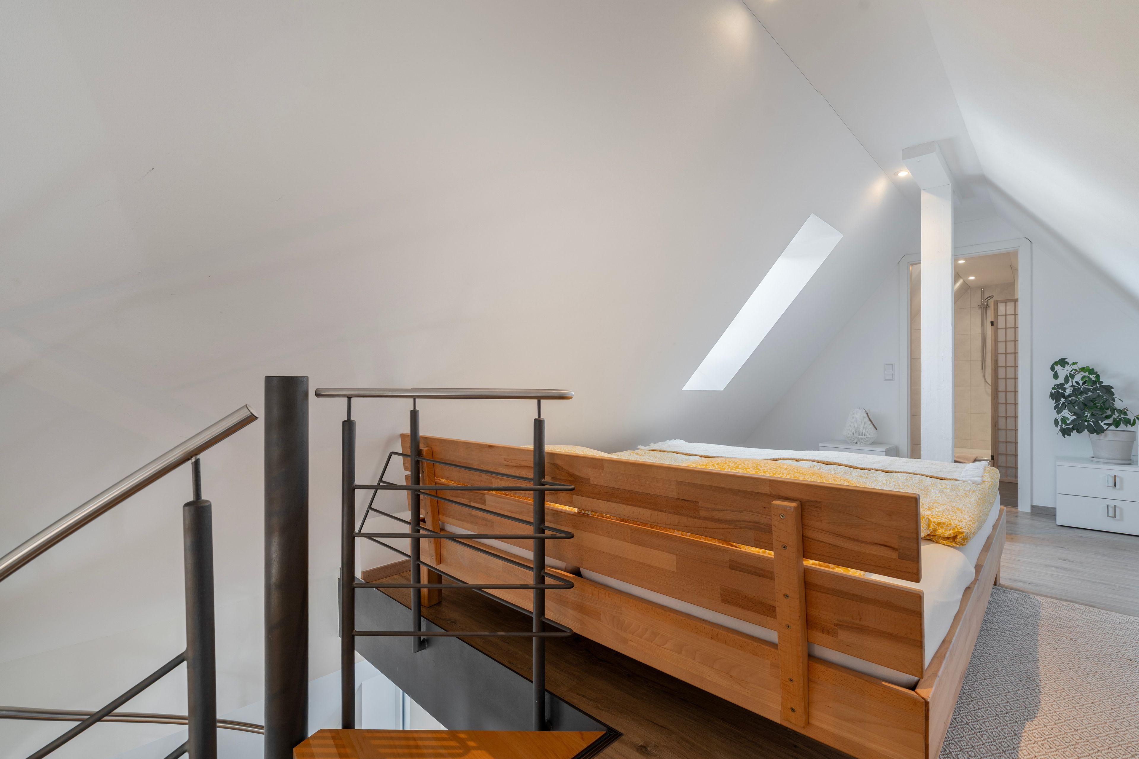 Een moderne loft slaapkamer met een schuine kap, een houten bed, een metalen trap en een dakraam.