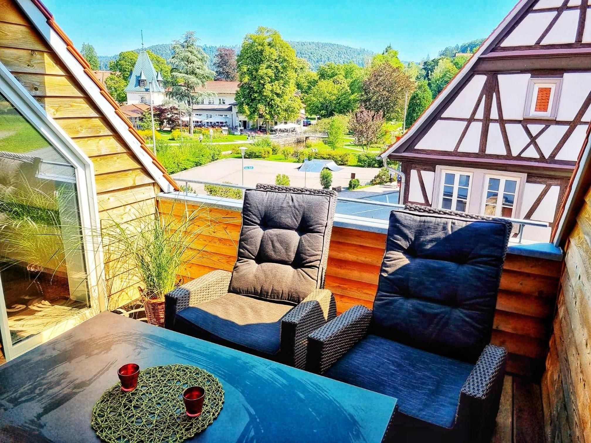 Ein Balkon mit zwei Stühlen, einem Tisch und Blick auf ein Dorf.