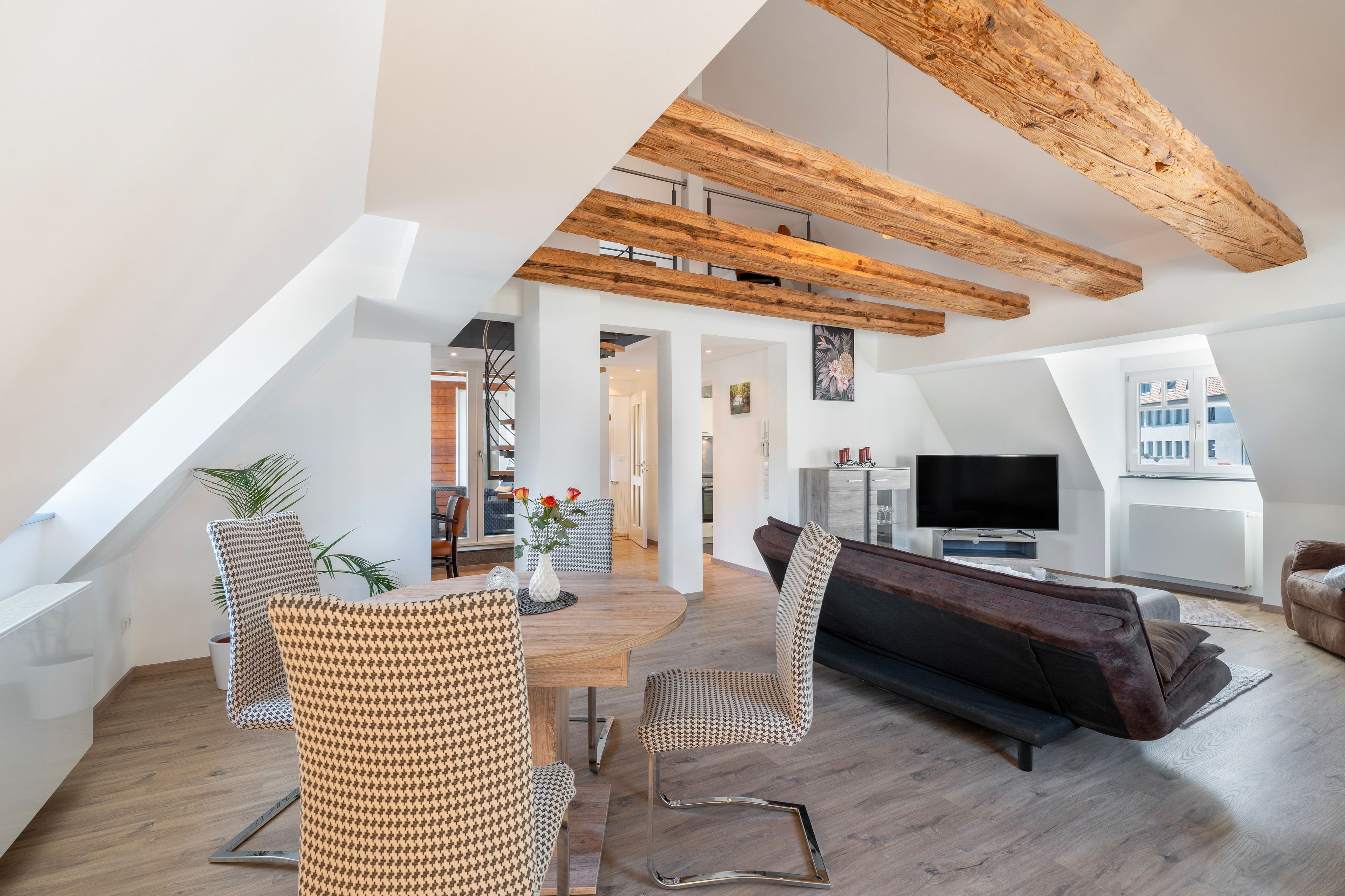 Eine moderne Loft-Wohnung mit freiliegenden Holzbalken, einer Essecke mit stuhlbezügen in Zickzackmuster, einem Sofa und einem Flachbildfernseher.