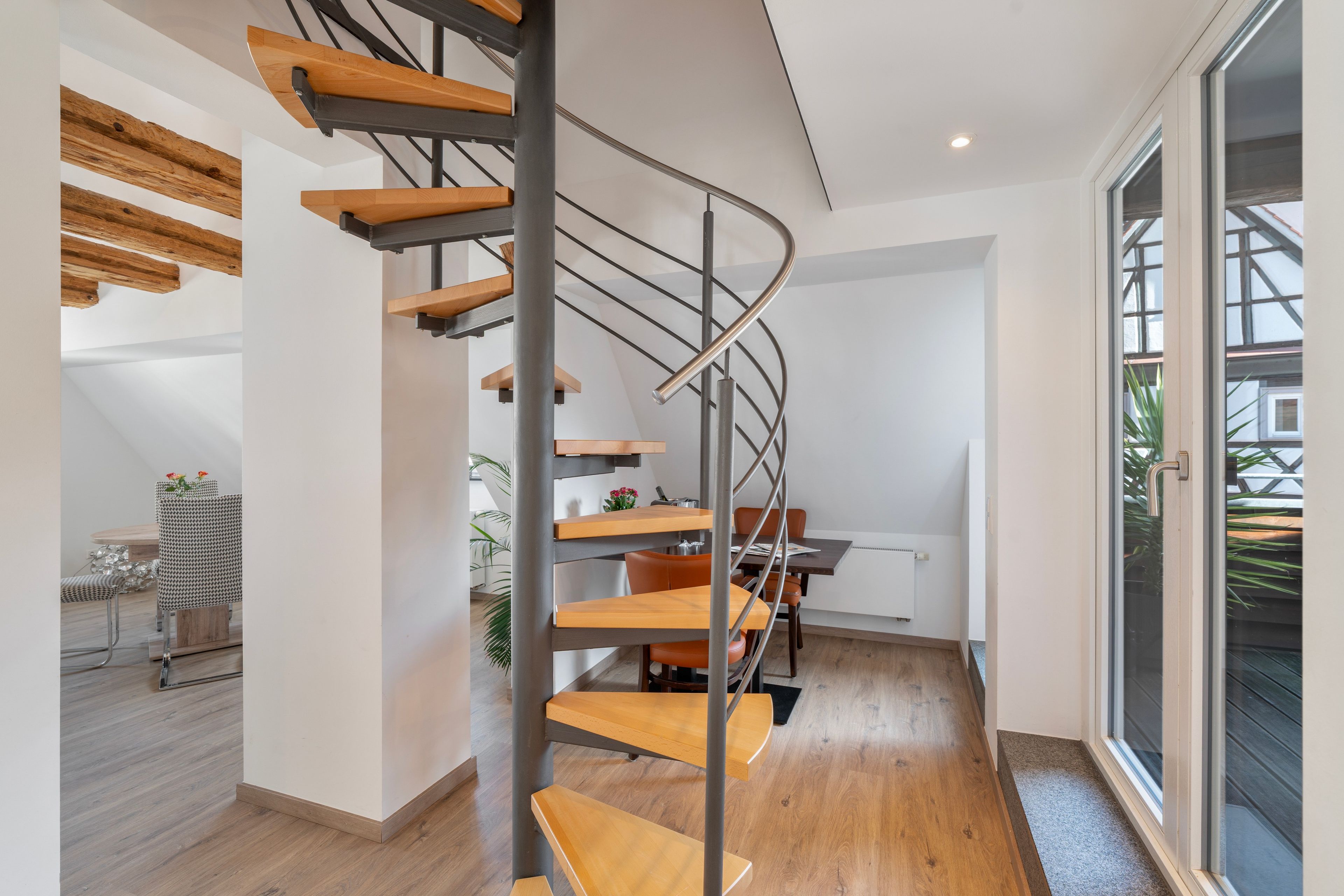 Ein modernes Interieur mit einer Wendeltreppe, Holzböden und einem Essbereich mit Stühlen und Tischen.