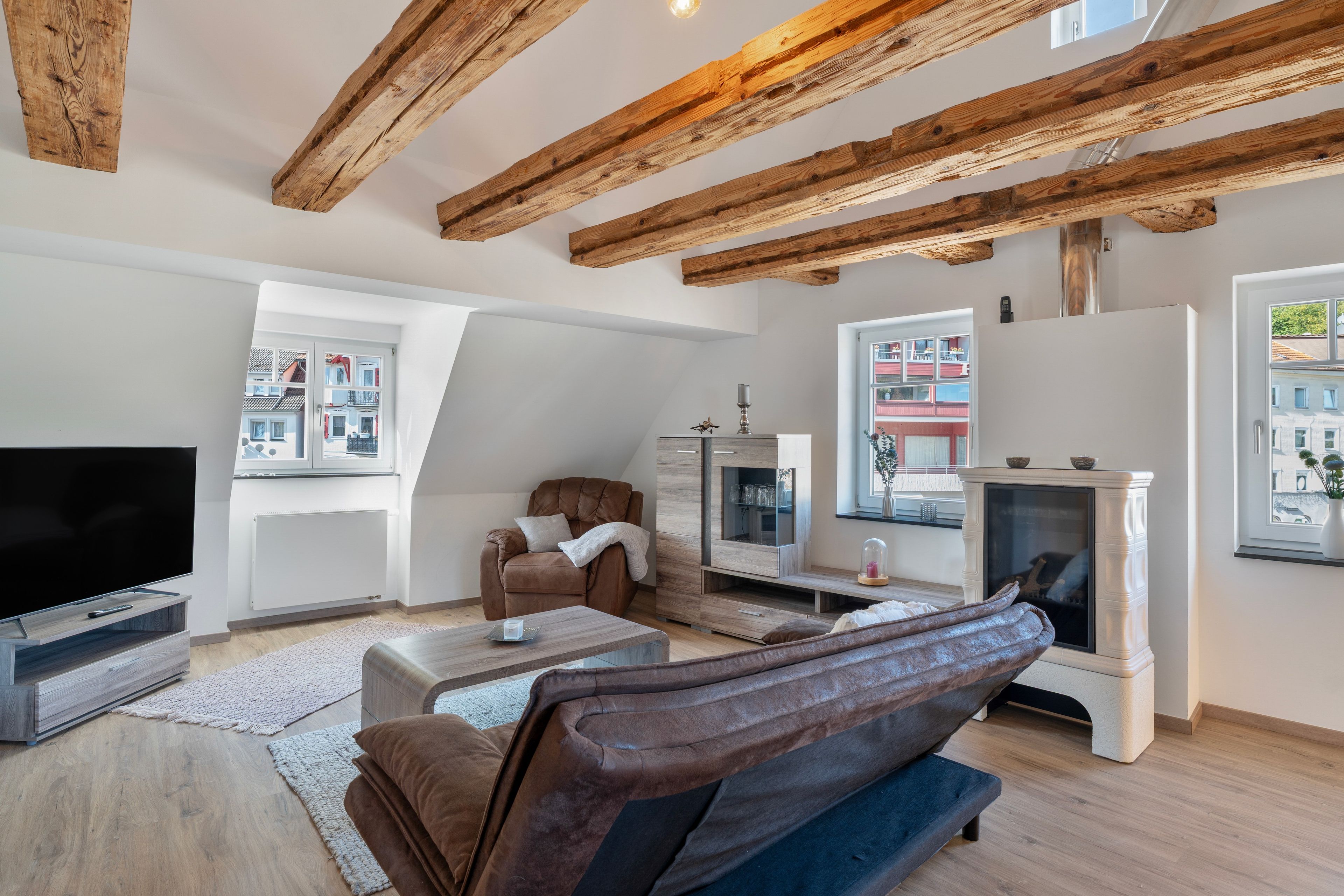 Ein modernes Wohnzimmer mit freiliegenden Holzbalken, einem Kamin, einem Fernseher und einem Sofa.