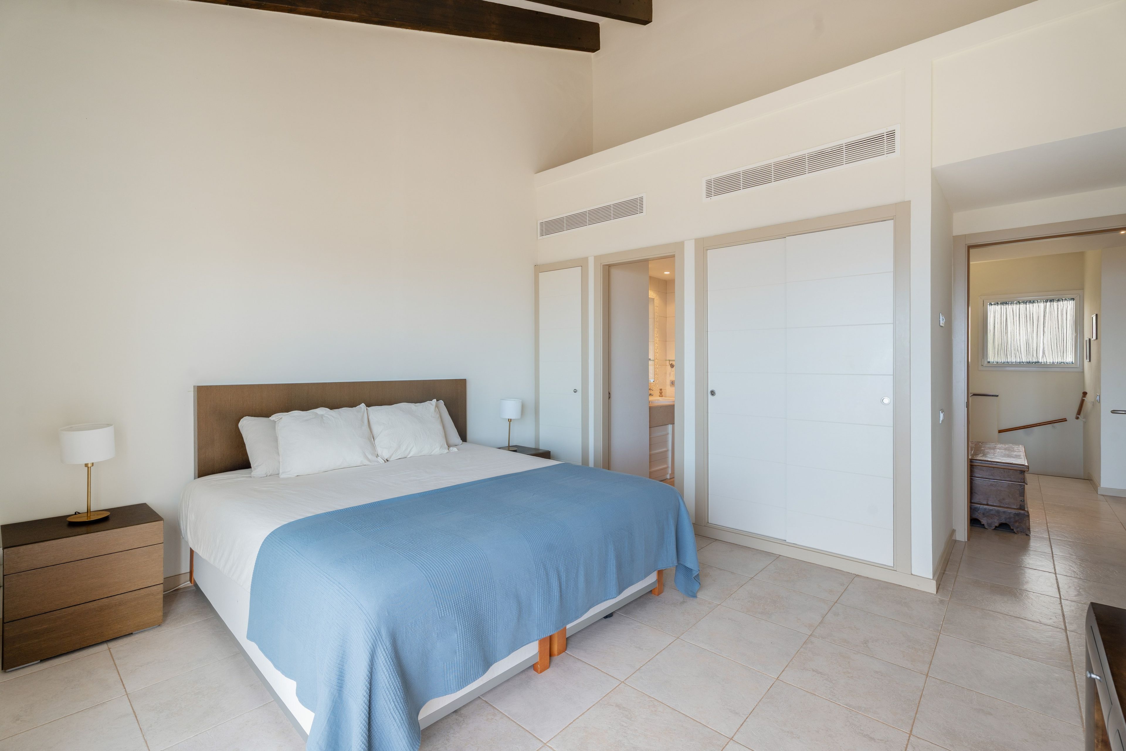 Une chambre à coucher avec un lit, des tables de chevet, une armoire et une salle de bain visible à travers une porte ouverte.
