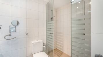 Un baño moderno con cabina de ducha de vidrio, un inodoro y un espejo.