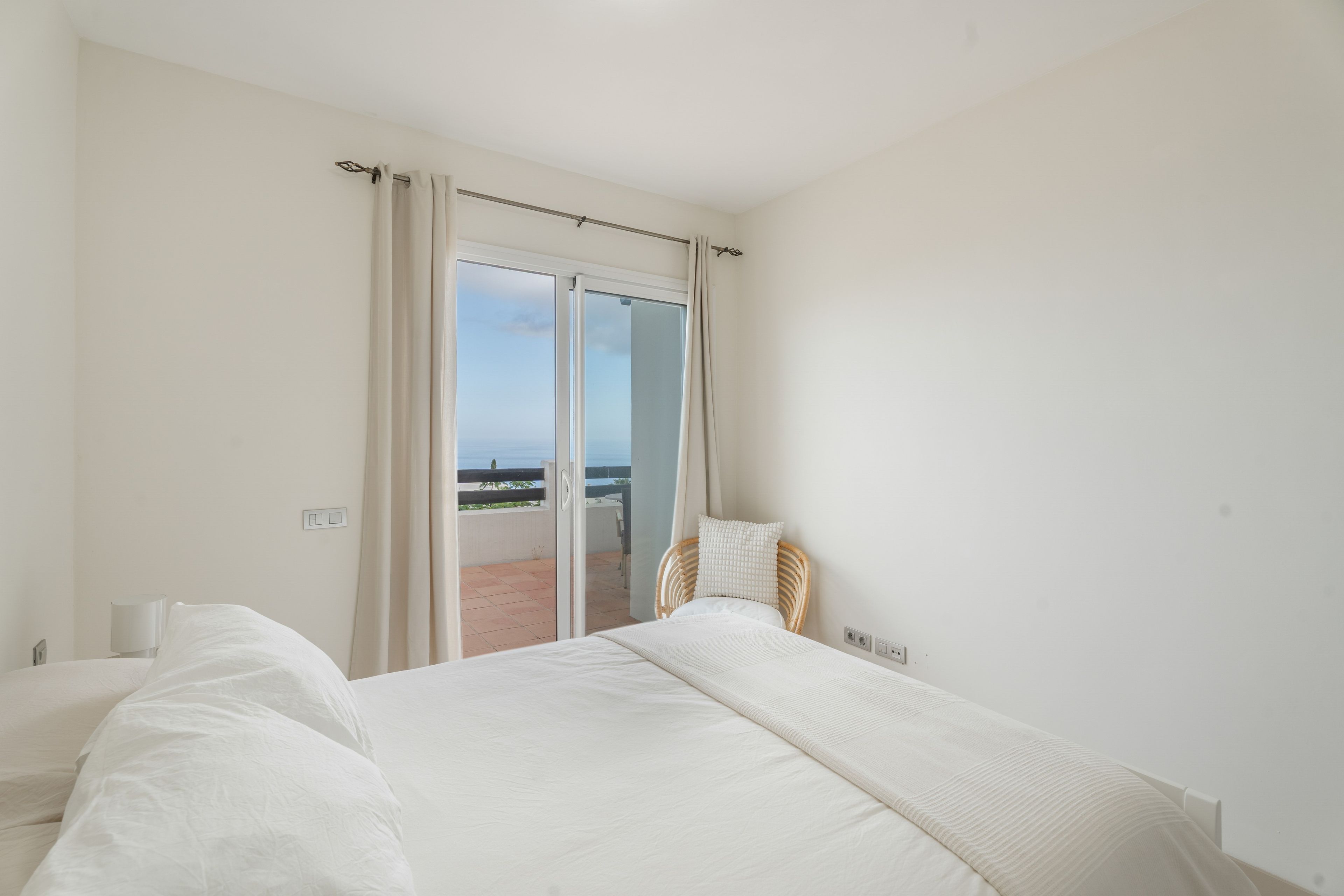 Un dormitorio con una cama grande, una silla y vistas al mar a través de una puerta corredera.
