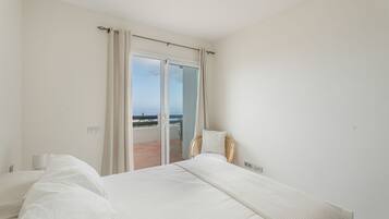 A bedroom with a large bed, a chair, and a view of the sea through a sliding door.
