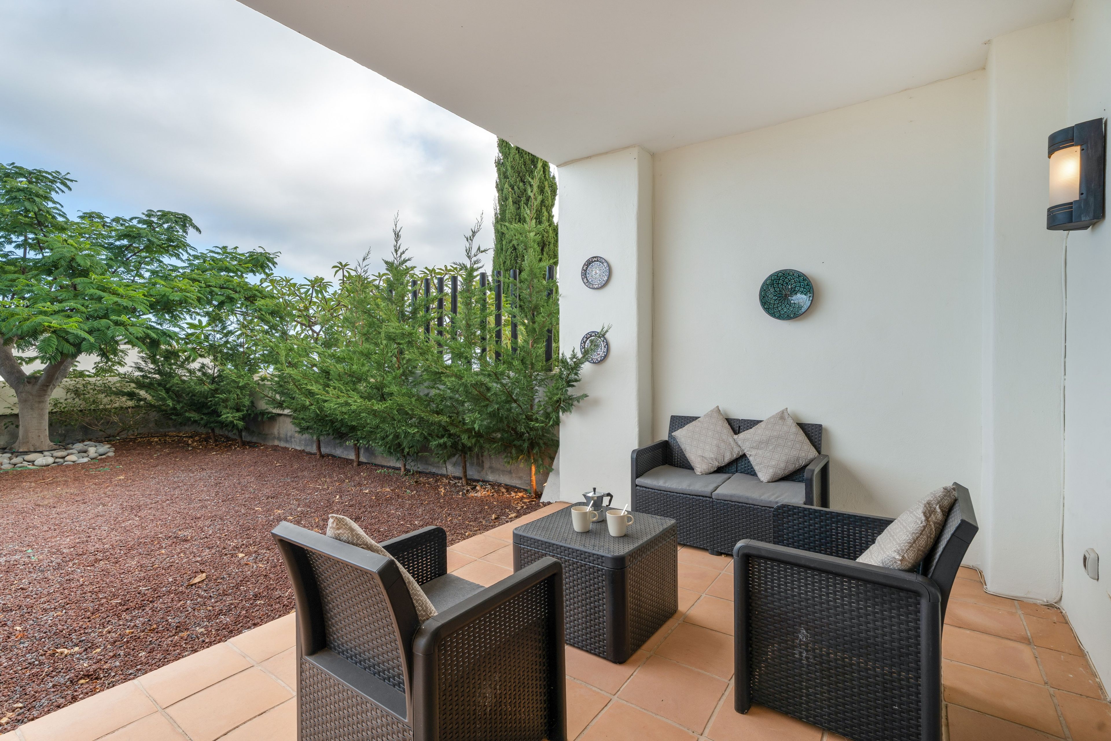 An outdoor patio with wicker furniture, a coffee table, and a wall-mounted light fixture.
