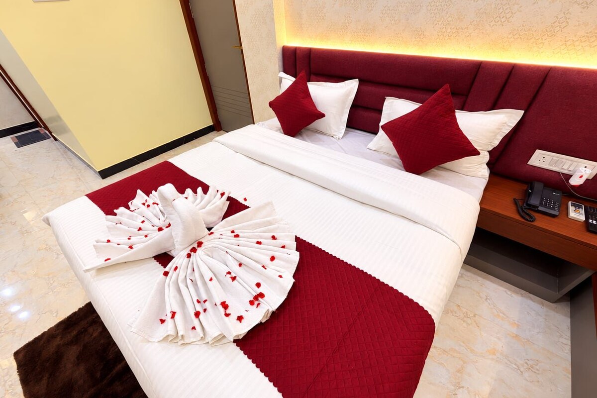 A hotel room with a neatly made bed, a red and white bedspread, a fluffy brown rug, and a bedside table with a phone and a power outlet.