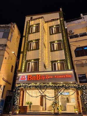 A multi-story hotel with a neon sign for 'BnB By Rama - Luxury Stay' and a reception area with a modern design. - BnB By Rama A Luxury Stay (Varanasi)