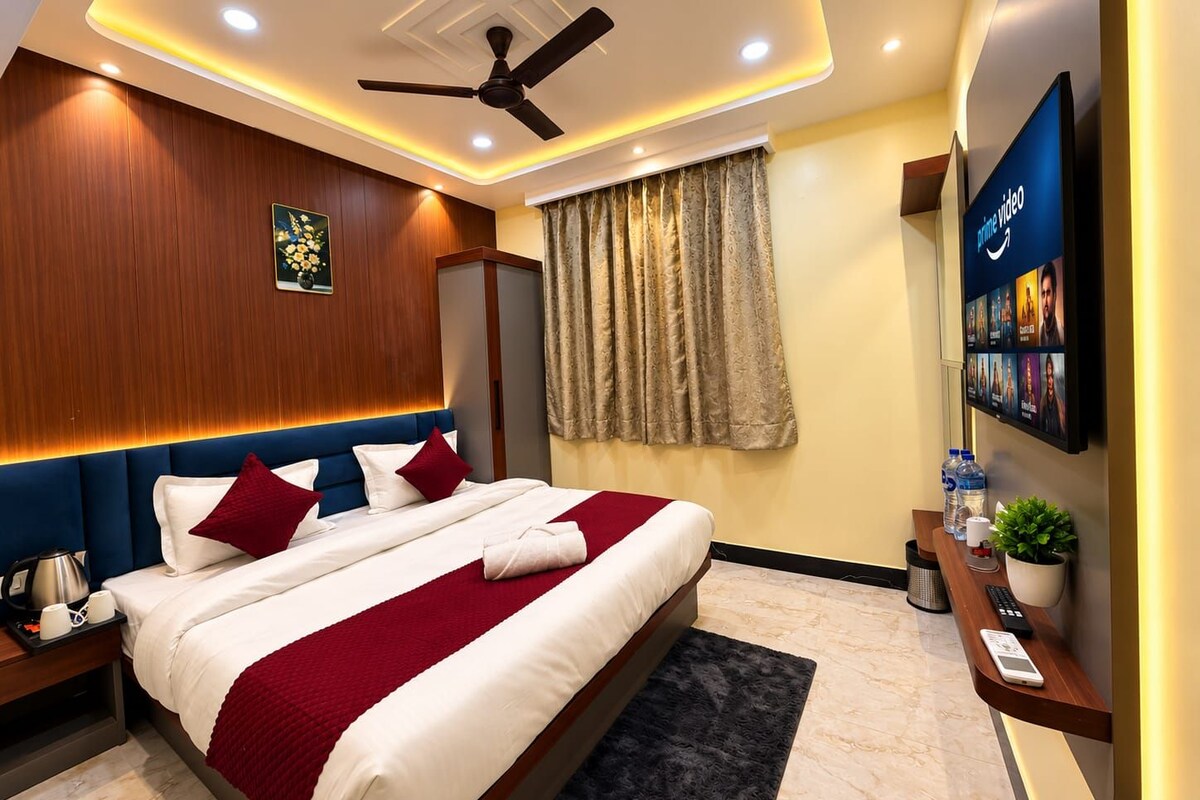 A hotel room with a bed, a ceiling fan, a TV, and a wall-mounted shelf with amenities.