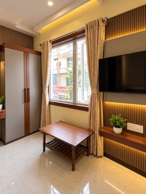 Une chambre moderne avec une table en bois, un téléviseur fixé au mur et une fenêtre avec des rideaux.