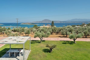 Eine Terrasse mit Tisch und Stühlen, Olivenbäumen und Blick auf Meer und Berge.