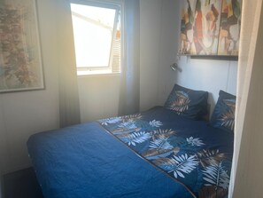 A bedroom with a bed, a window, and a wall-mounted artwork. - Mobile home in a quiet area of the 4-star campground; 100 meters from the beach (Marseillan)