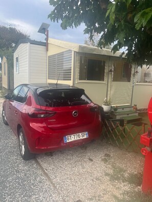 A red car parked in front of a building with a solar panel on the roof. - Mobile home in a quiet area of the 4-star campground; 100 meters from the beach (Marseillan)