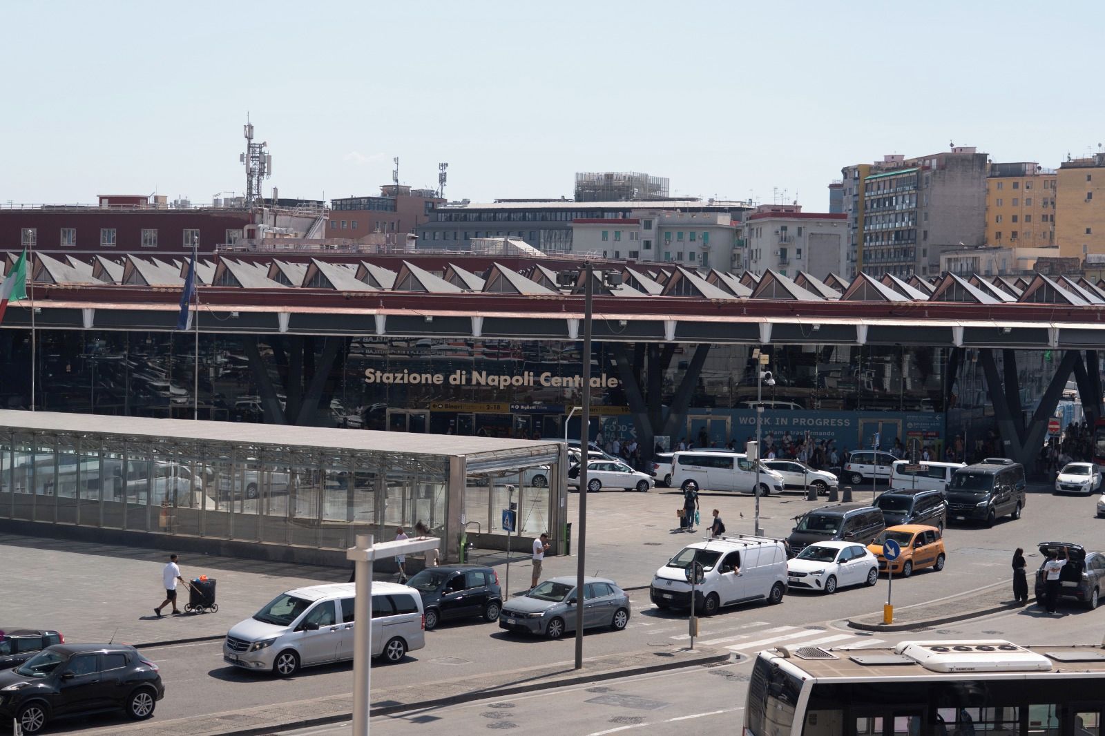 Une rue animée en plein centre-ville, avec un grand bâtiment en verre portant l’inscription « Stazione di Napoli Centrale ».