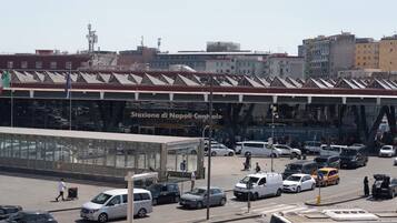Une rue animée en plein centre-ville, avec un grand bâtiment en verre portant l’inscription « Stazione di Napoli Centrale ».