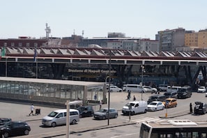 Une rue animée en plein centre-ville, avec un grand bâtiment en verre portant l’inscription « Stazione di Napoli Centrale ».
