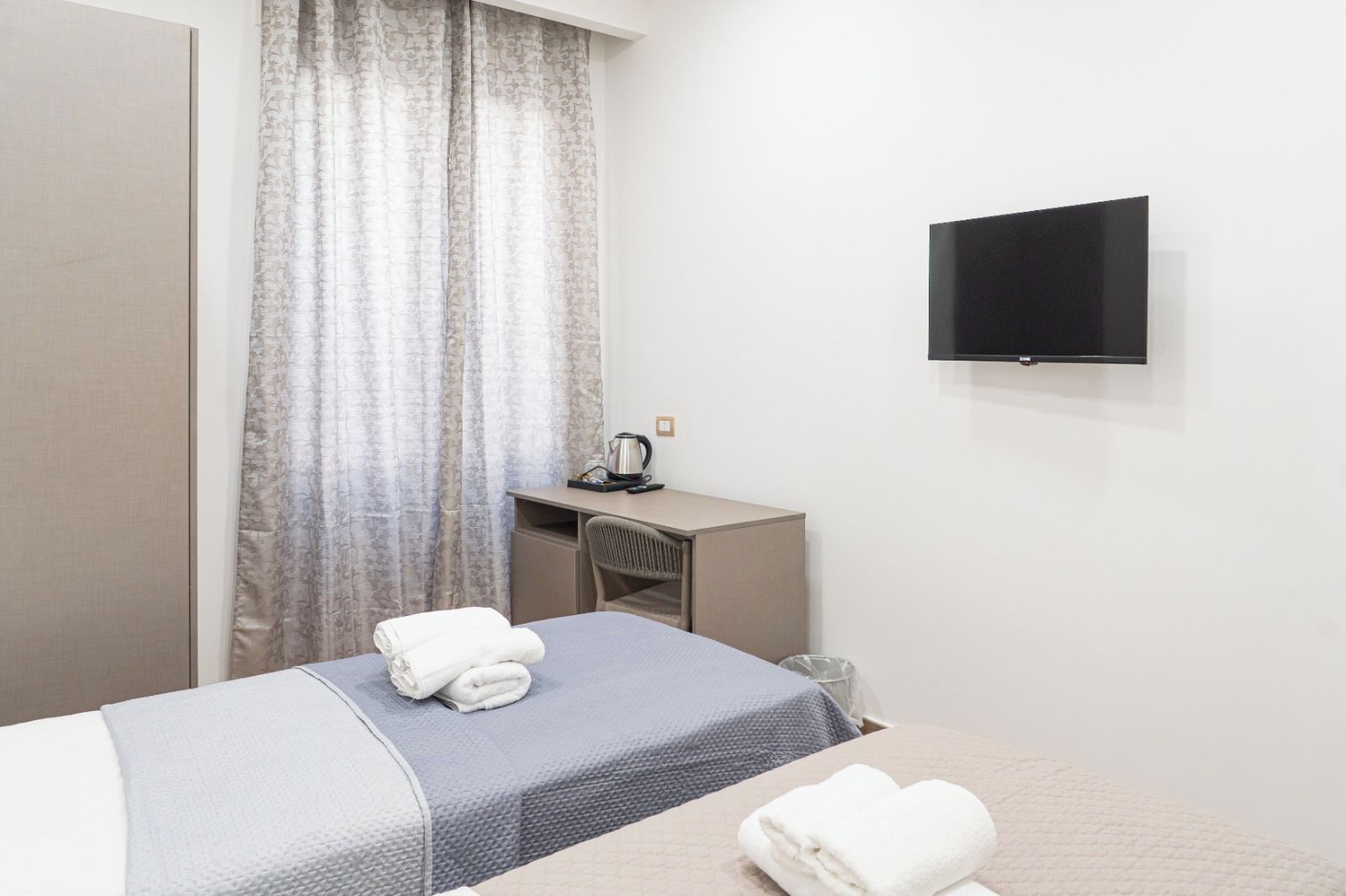 Une chambre d’hôtel avec un lit, un bureau, une chaise, une télévision et une fenêtre avec des rideaux.