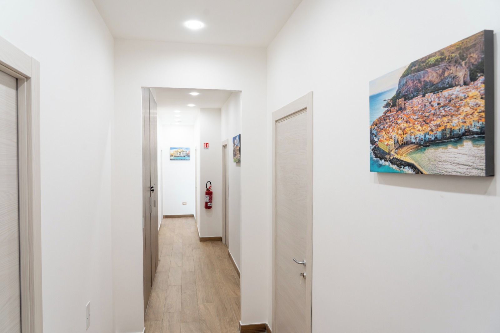 Ein Korridor mit einem an der Wand befestigten Feuerlöscher, einer Tür am Ende und einem Gemälde an der Wand.