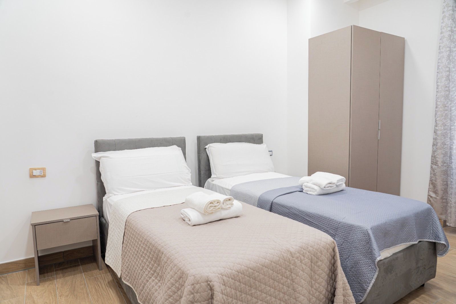A hotel room with two beds, a wardrobe, and a nightstand.