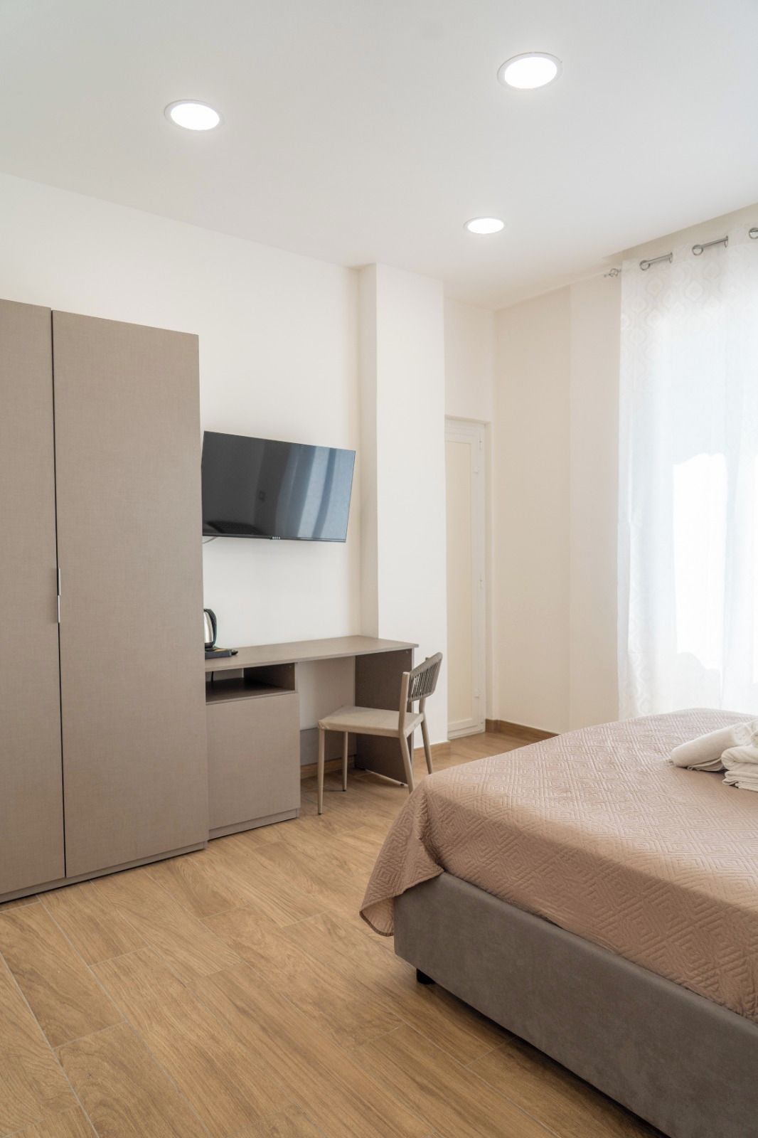 Une chambre à coucher avec un lit, un bureau, une chaise, une armoire et un téléviseur fixé au mur.
