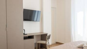 Une chambre à coucher avec un lit, un bureau, une chaise, une armoire et un téléviseur fixé au mur.