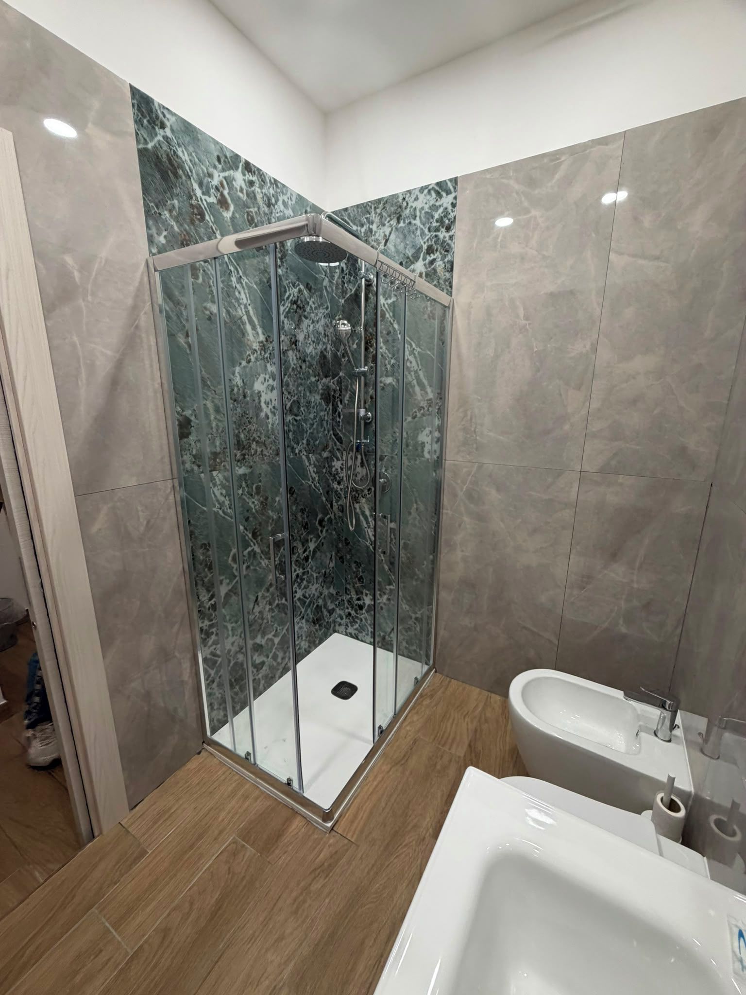 Ein modernes Badezimmer mit einer in Glas abgeschirmten Dusche, einem weißen Waschbecken und Marmorwänden.