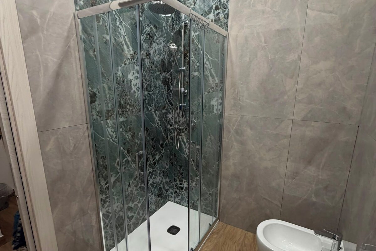 Une salle de bain moderne avec une douche à parois de verre, un lavabo blanc et des murs en marbre.