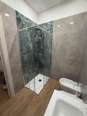 Une salle de bain moderne avec une douche à parois de verre, un lavabo blanc et des murs en marbre.