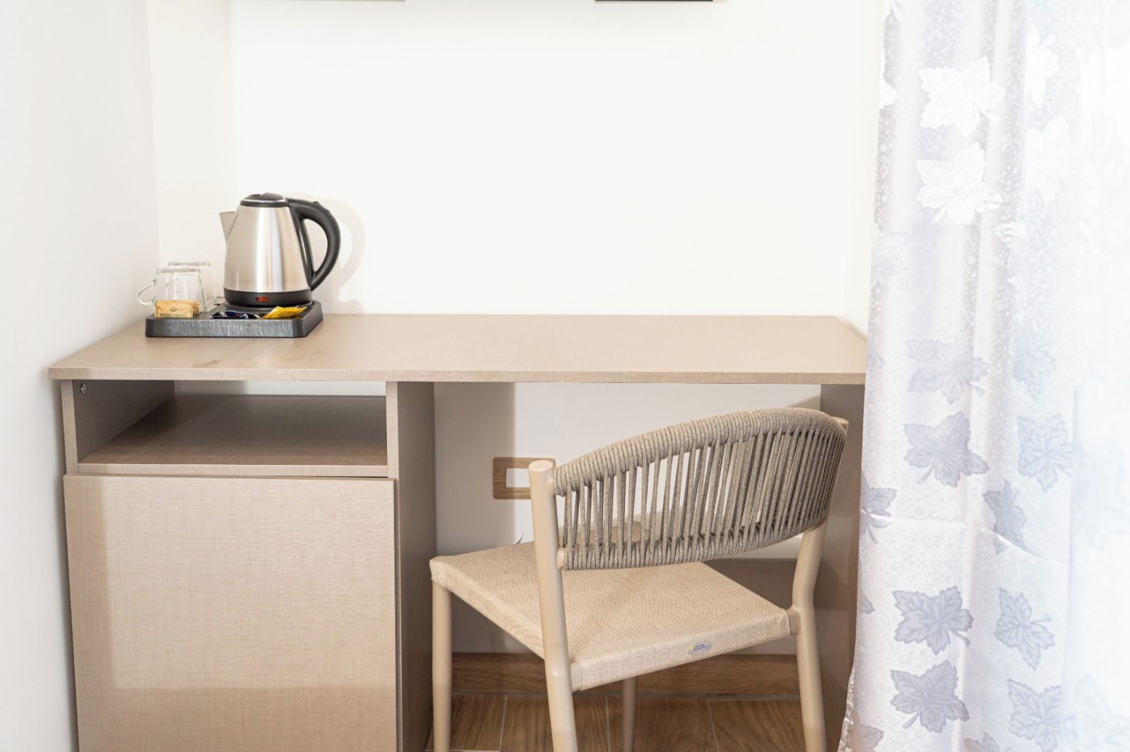 Un espacio de trabajo funcional con un escritorio de madera, una silla, un hervidor y un refrigerador pequeño.