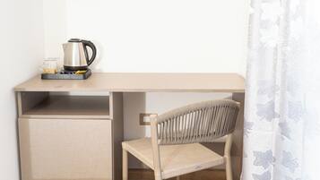 Un espacio de trabajo funcional con un escritorio de madera, una silla, un hervidor y un refrigerador pequeño.