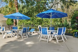 Terrassenmöbel im Freien mit blauen Sonnenschirmen, weißen Stühlen und einem Betonboden.