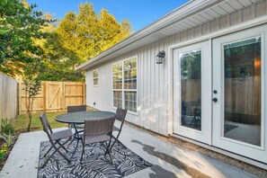 A patio with a round table and chairs, a wooden fence, and a house with white siding and large windows. - University South Alabama Home Windham (Mobile)