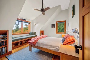 Ein Schlafzimmer mit Bett, Fensterbank, Bücherregal und Deckenventilator.
