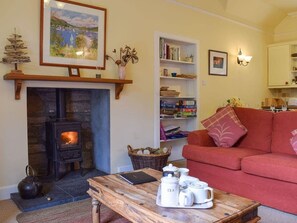 A cozy living room with a fireplace, a red sofa, a bookshelf, and a coffee table with tea set. - Glebe Cottage | 2 Bedroom Cottage in Perthshire (Scone)